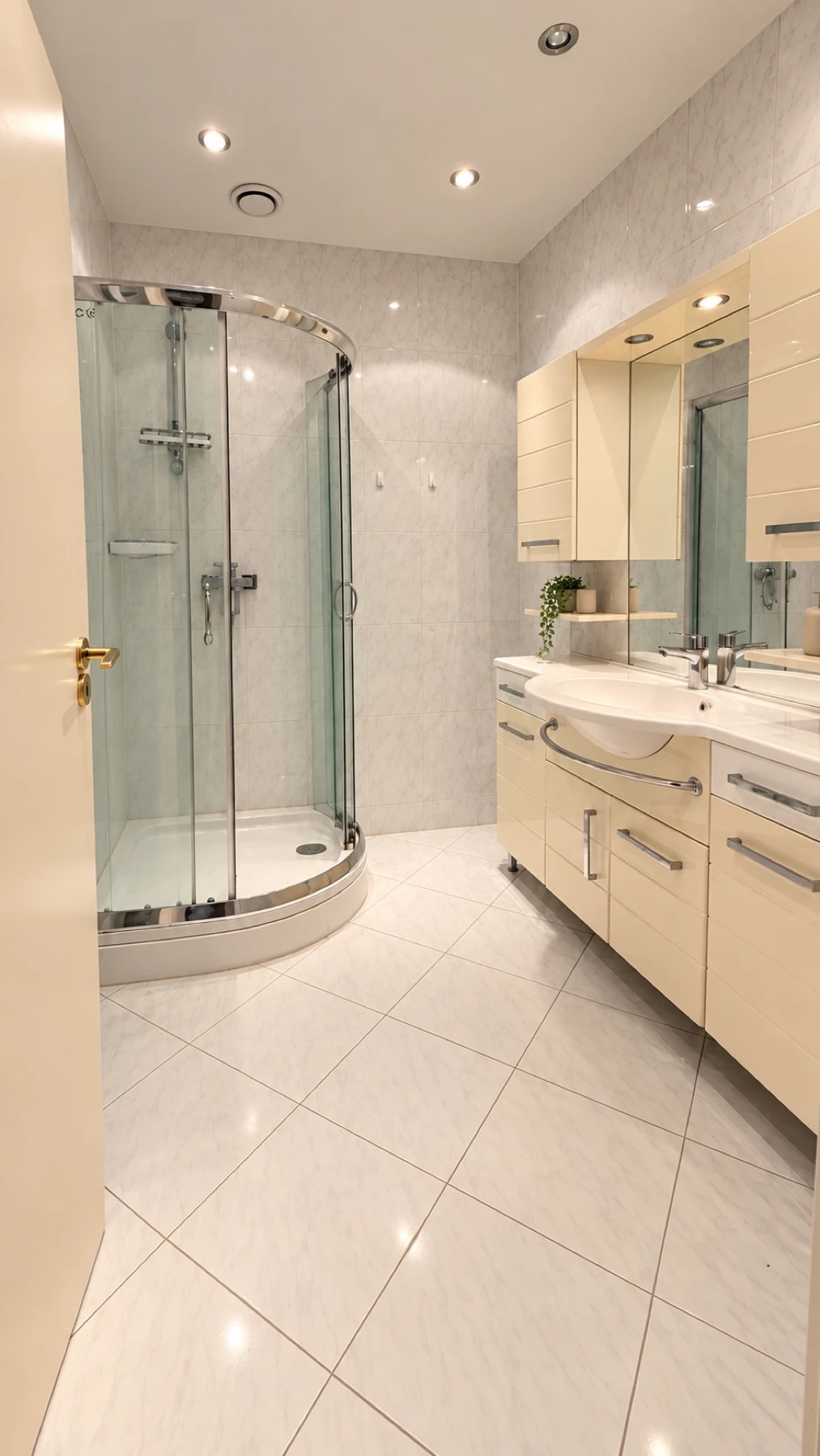 Bathroom with a quarter-round shower cabin, cream vanity units and a lit mirror cabinet